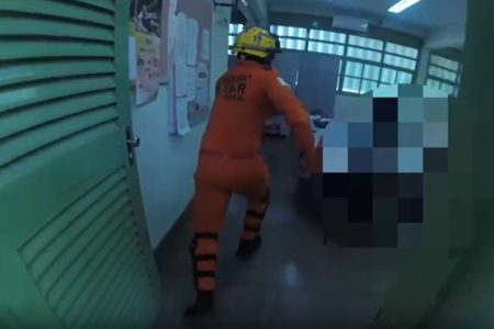 Imagem colorida de um bombeiro correndo em uma sala de aula de porta verde