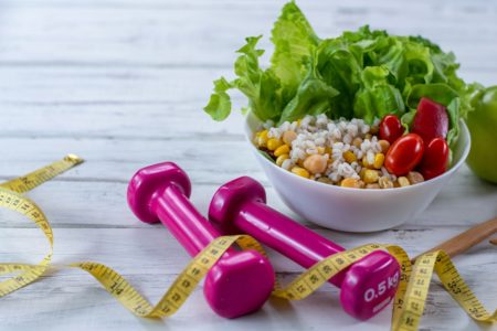 Foto de Conceito de estilo de vida saudável. Haltere, salada de legumes e fita métrica na mesa de madeira rústica.