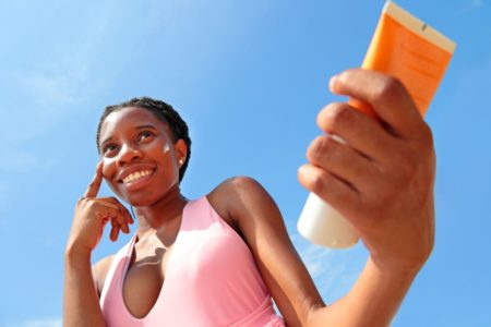 Foto colorida de uma menina passando protetor solar no sol - Metrópoles