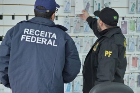 Foto colorida de agentes da receita federal e da polícia federal recolhendo produtos clandestinos - Metrópoles
