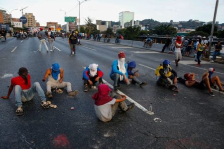 Manifestantes com os rostos cobertos sentam-se em rua de Caracas - Metrópoles