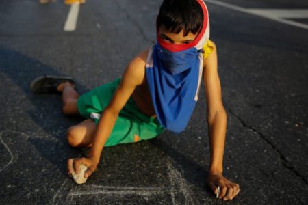 Um jovem manifestante escreve slogans na calçada durante protesto contra o governo de Nicolás Maduro nas ruas de Caracas, em 2 de fevereiro de 2019 - Metrópoles