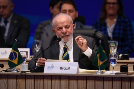 Imagem colorida do presidente Lula em evento do G20, falando em microfone e com plaqueta do Brasil - Metrópoles