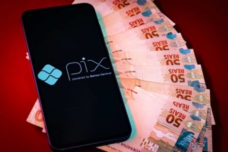 Imagem colorida mão com dinheiro e aplicativo PIx dinheiro pagamento moeda digital - Metrópoles