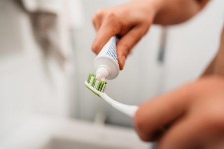 Close de um jovem colocando pasta de dente em uma escova de dentes para escovar os dentes no banheiro pela manhã.