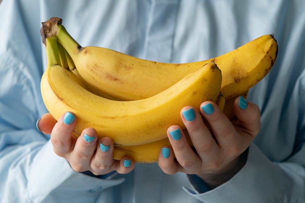 Foto colorida: Mulher com um cacho de banana na mão