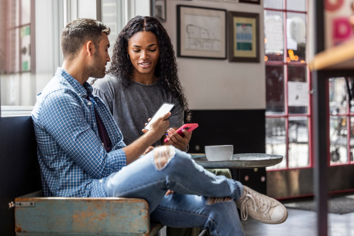 um homem branco e uma mulher negra conversando com os celulares na mão