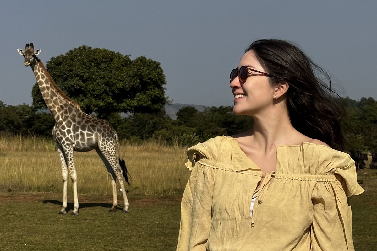 Foto colorida de mulher tirando foto perto de uma girafa - Metrópoles