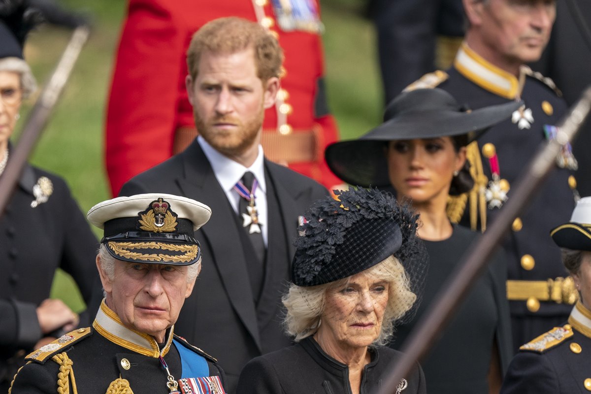 Foto colorida de homens com traje militar britânico e outros com blazer preto. Há mulheres com roupas e chapéus pretos - Metrópoles