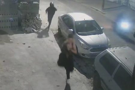 Mulher com roupa de lycra corre em calçada, perseguida por homem de capacete, no período noturno - Metrópoles
