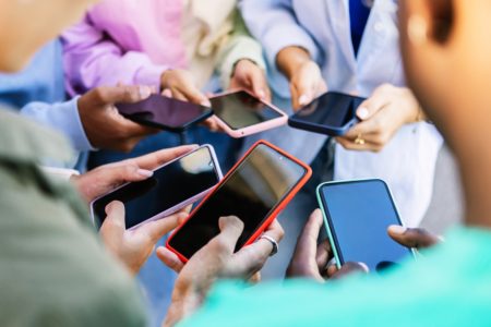 Imagem colorida de jovens mexendo no celular juntos - Metrópoles
