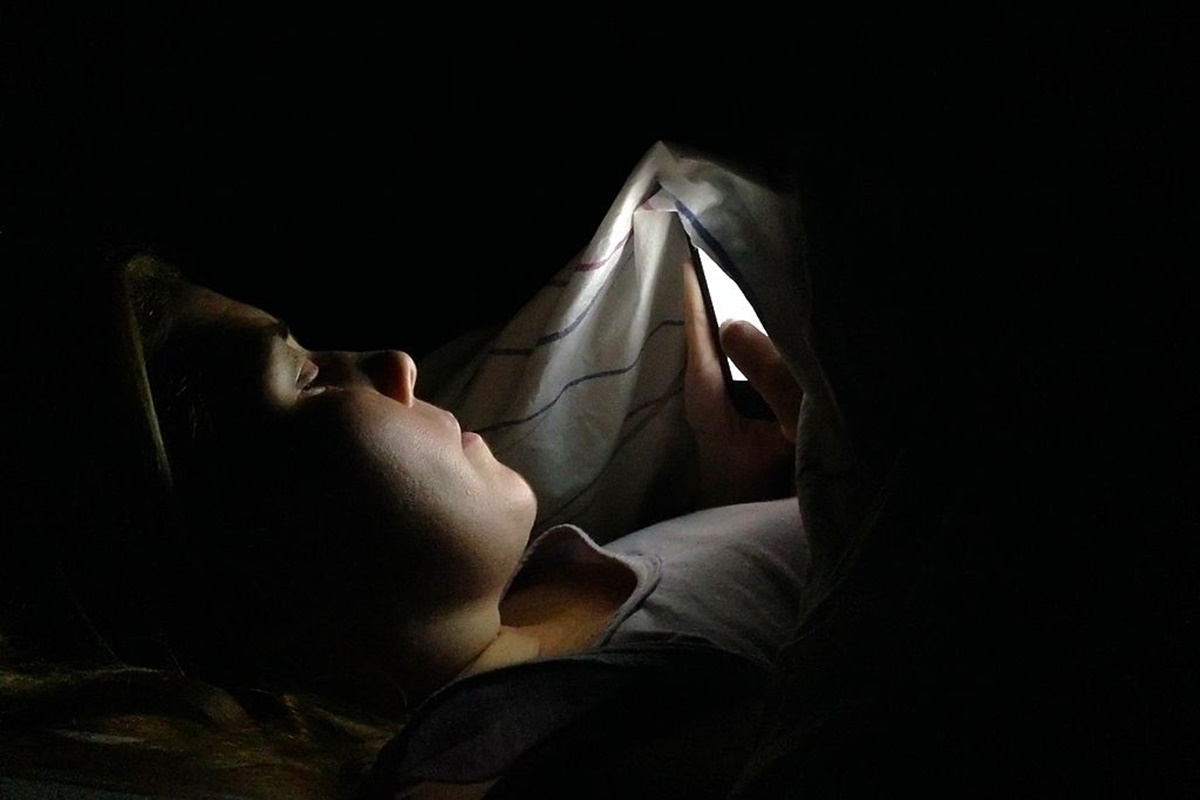 Imagem colorida de mulher mexendo no celular no escuro - Metrópoles