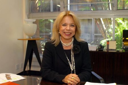 Vice-reitora da USP Maria Arminda do Nascimento com terno preto e colares. Ela tem cabelos loiros e está sentada- Metrópoles