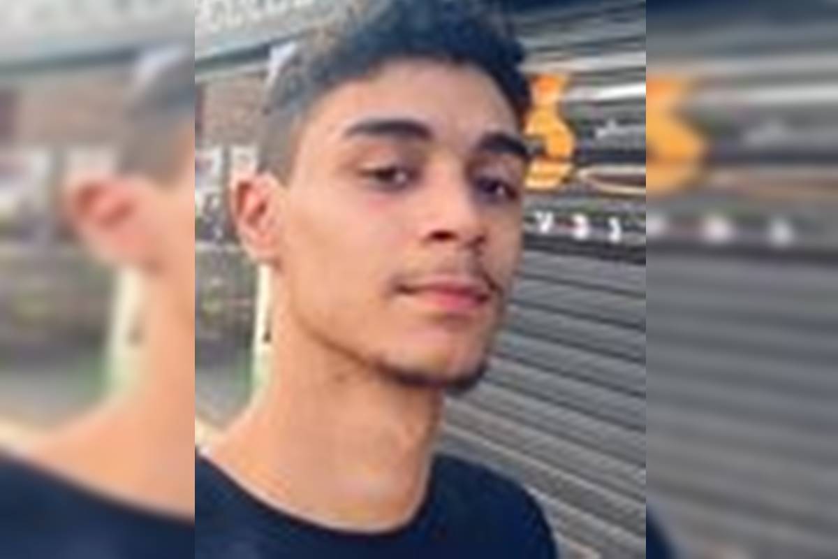 Imagem colorida de um jovem branco, de cabelos pretos curtos e cavanhaque. Ele veste camiseta preta