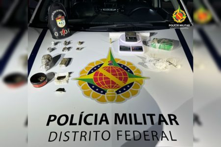 Imagem colorida de porções de drogas diversas e uma balança de precisão sobre uma viatura da PMDF