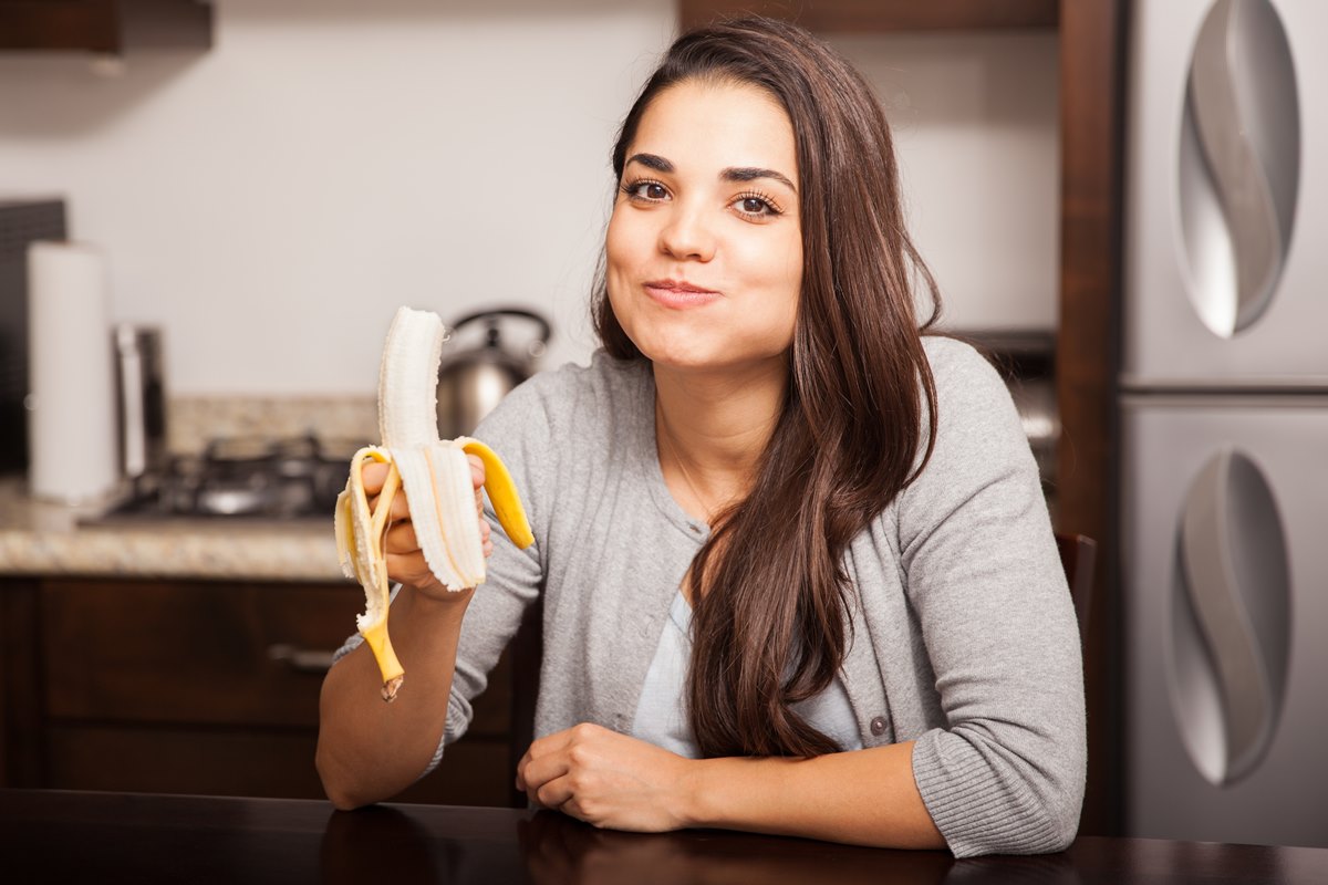 Foto colorida de mulher comendo banana - Metrópoles