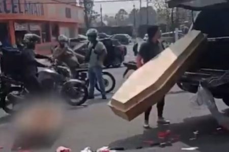 Imagem colorida de homem segurando tampa de caixão enquanto restante está no chão com o corpo. Metrópoles