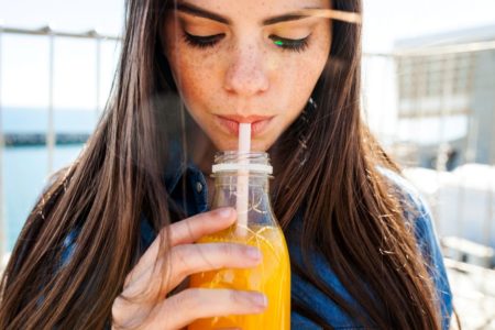 mulher de cabelo escuro tomando um suco laranja