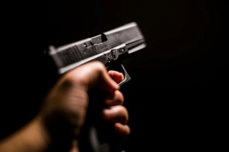 Imagem colorida de uma mão apontando uma arma de fogo - Metrópoles
