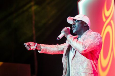 foto colorida do cantor Akon de roupa branca em cima do palco