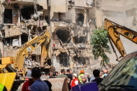Foto colorida de equipes de resgate vasculhando escombros em local de um ataque israelense - Metrópoles