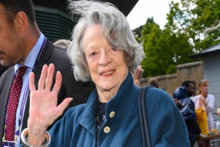 Imagem colorida da atriz Maggie Smith, sorrindo e acenando para a câmera com roupa azul - Metrópoles