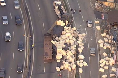Imagem aérea mostra caminhão tombado em pista de rodovia com carregamento de várias grandes caixas brancas espalhadas pela pista -Metrópoles