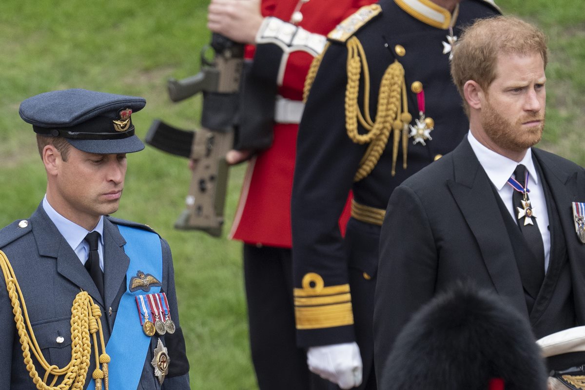 Foto colorida de homem com traje militar britânico ao lado de homem com terno preto - Metrópoles