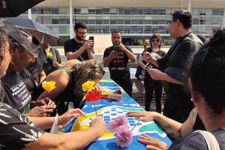 Imagem colorida de pessoas ao redor de caixão em manifestação do INSS - Metrópoles