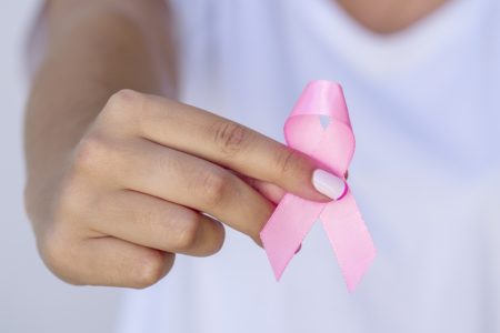 Foto da mão de uma mulher segurando a fita rosa e usa camisa para apoiar a vida e a doença das pessoas. com câncer de mama Metrópoles