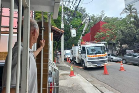 Morador observa caminhão da Enel trabalhando na região do Guarapiranga, zona sul de São Paulo