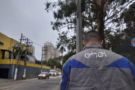Imagens coloridas mostram funcionário com uniforme da empresa Enel, de costas, do lado direito, e do lado esquerdo, carros segundo no sentido contrário ao homem