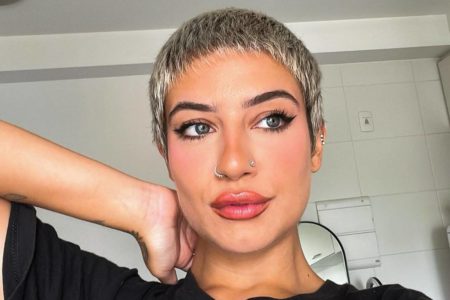 Imagem colorida da Cantora Clau com a mão no pescoço, olhando para o lado - Metrópoles