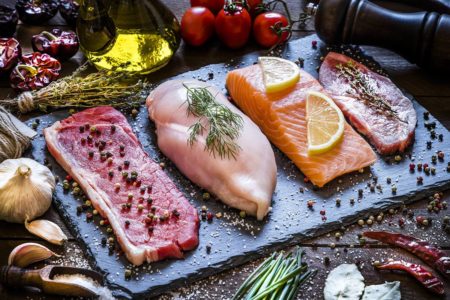 Foto colorida de filés de carne bovina, frango, peixe e suína em cima de uma tábua. As carnes estão rodeadas de temperos e vegetais - Metrópoles