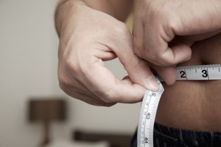 Imagem mostra um homem medindo a própria barriga com uma fita métrica branca - Metrópoles