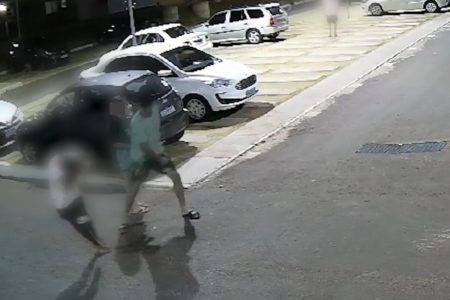 Imagem colorida de um homem agredindo um adolescente com um soco no rosto. Outra adolescente está ao lado na cena. No fundo, há carros e prédios