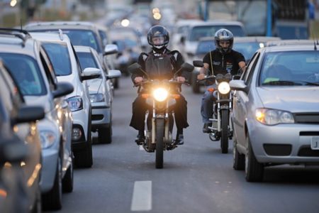 Motociclista entre carros em uma rua