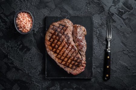 Na imagem colorida, uma carne grelhada é disposta em um fundo preto - Metrópoles