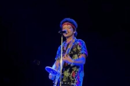 foto colorida de Bruno Mars cantando e segurando raquete elétrica - metrópoles