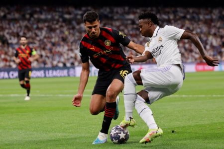Foto colorida de Rodri e Vini Jr. em disputa de bola durante partida da Champions League - Metrópoles
