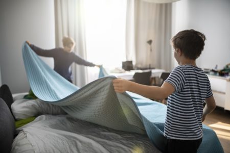 Imagem mostra duas crianças esticando um lençol azul para arrumaar a cama - Metrópoles