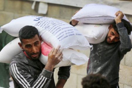 Foto colorida de palestinos carregando sacos de farinha, em Gaza - Metrópoles