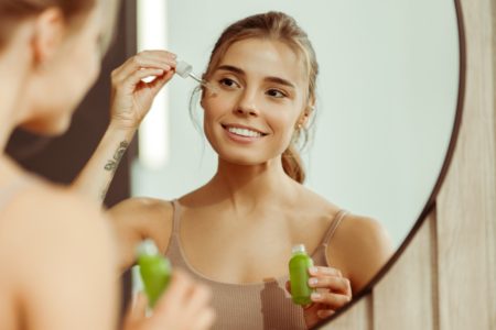 Foto colorida de mulher fazendo rotina de skincare em frente a um espelho - Metrópoles