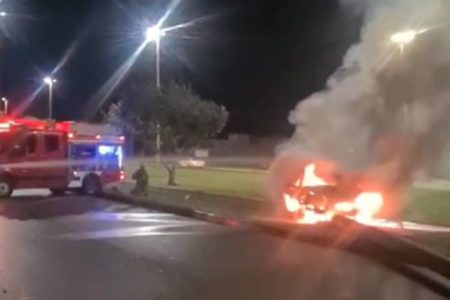 Carro pegando fogo e viatura do corpo de bombeiros ao fundo. Há muita fumaça no local - Metrópoles
