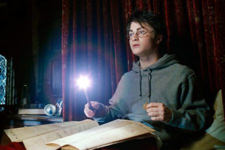 FOTO COLORIDA DE HARRY POTTER SENTADO COM VARINHA ACESA SOBRE PAPEL - METRÓPOLES