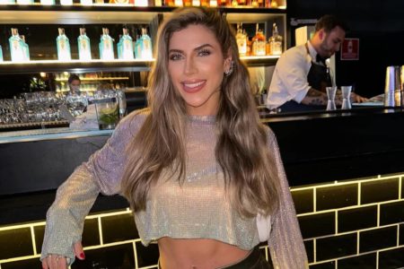 Imagem colorida de mulher em bar, poando para a foto sorrindo e com blusa cintilante - Metrópoles