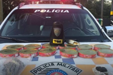 Imagem colorida de latas de sardinha com cocaína em cima de viatura da polícia militar. Metrópoles