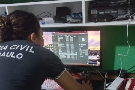 Imagem colorida de mulher mexendo em computador apreendido. Metrópoles
