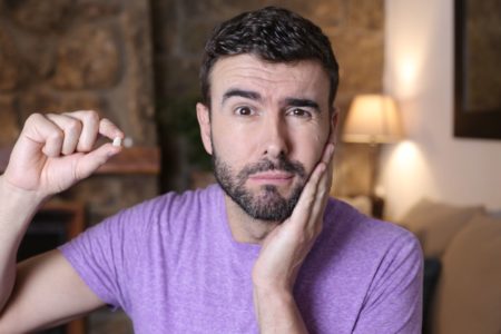 Homem com dente na mão e a mão no rosto sonhar com dente caindo