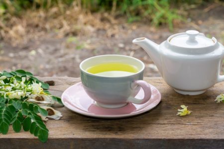Chá de Moringa em xícara e folhas verdes frescas, flores e sementes com bule em madeira, desfocar o fundo. Moringa oleifera erva tropical conceito de estilo de vida saudável.